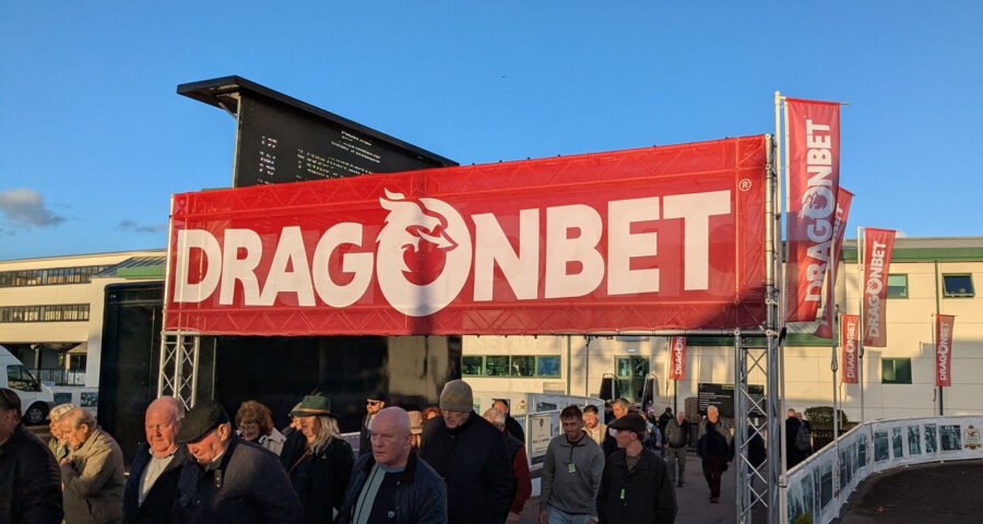 Photo of punters leaving a racecourse, walking under a banner displaying the word 'DragonBet'.